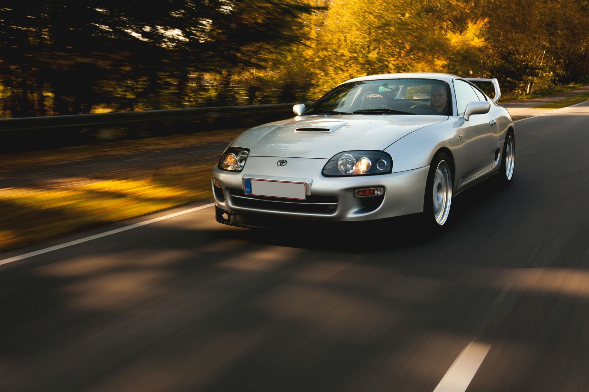 White sports car driving on a curving road with autumn trees in the background