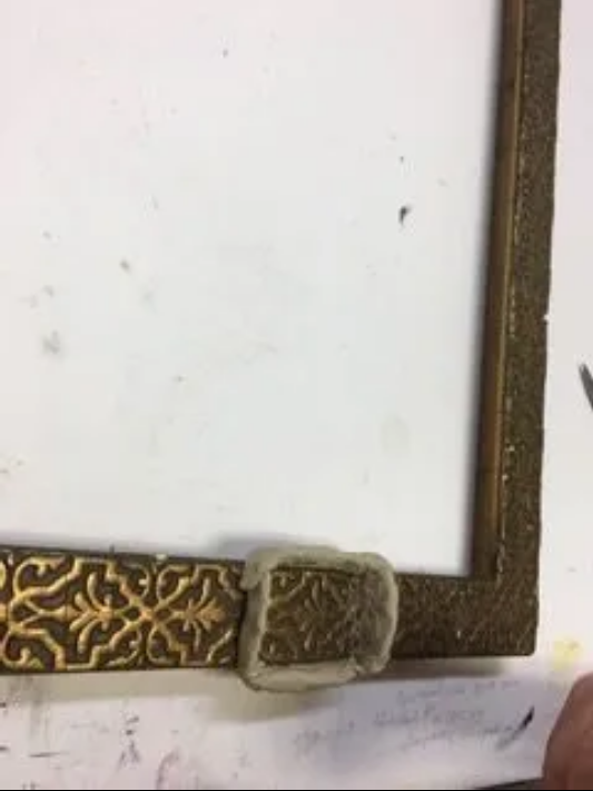 A picture frame with a gold buckle is sitting on a white surface.
