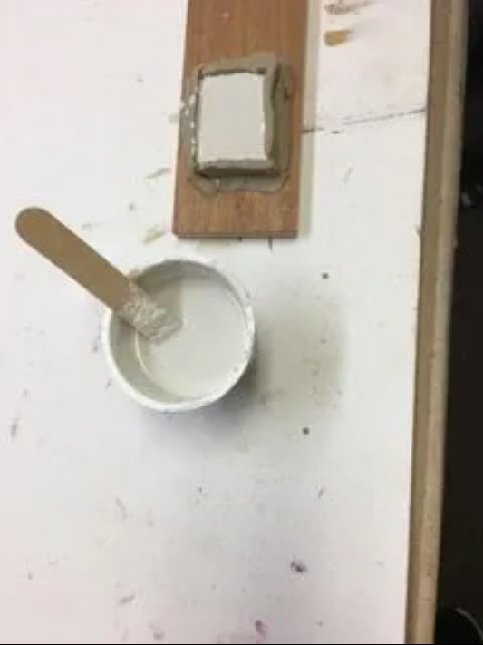 A bowl of white paint and a spoon on a table.