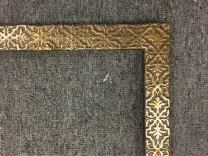 A gold frame with a pattern on it is sitting on a gray surface.