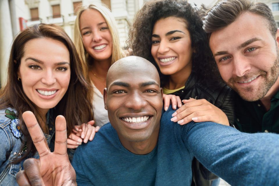 Smiling group taking a selfie outdoors, with one person making a peace sign