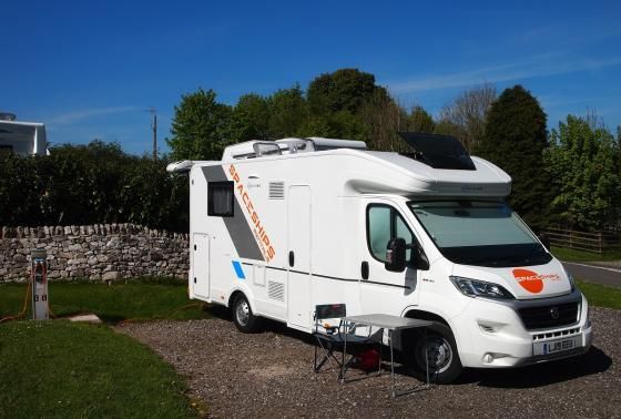 A white rv is parked in a gravel area next to a stone wall.