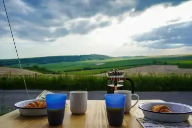 A table with a view of a field and a bowl of croissants on it.
