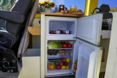 A small refrigerator filled with fruits and vegetables in a van.