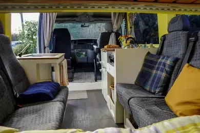 The inside of a camper van with a bed and chairs.