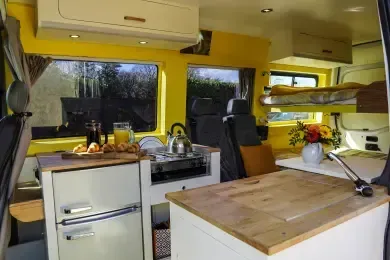A kitchen in a van with yellow walls and a wooden counter top.