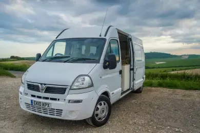 A white van is parked on the side of the road in a field.
