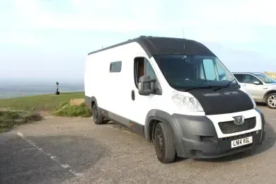 A white van with a black hood is parked in a parking lot.
