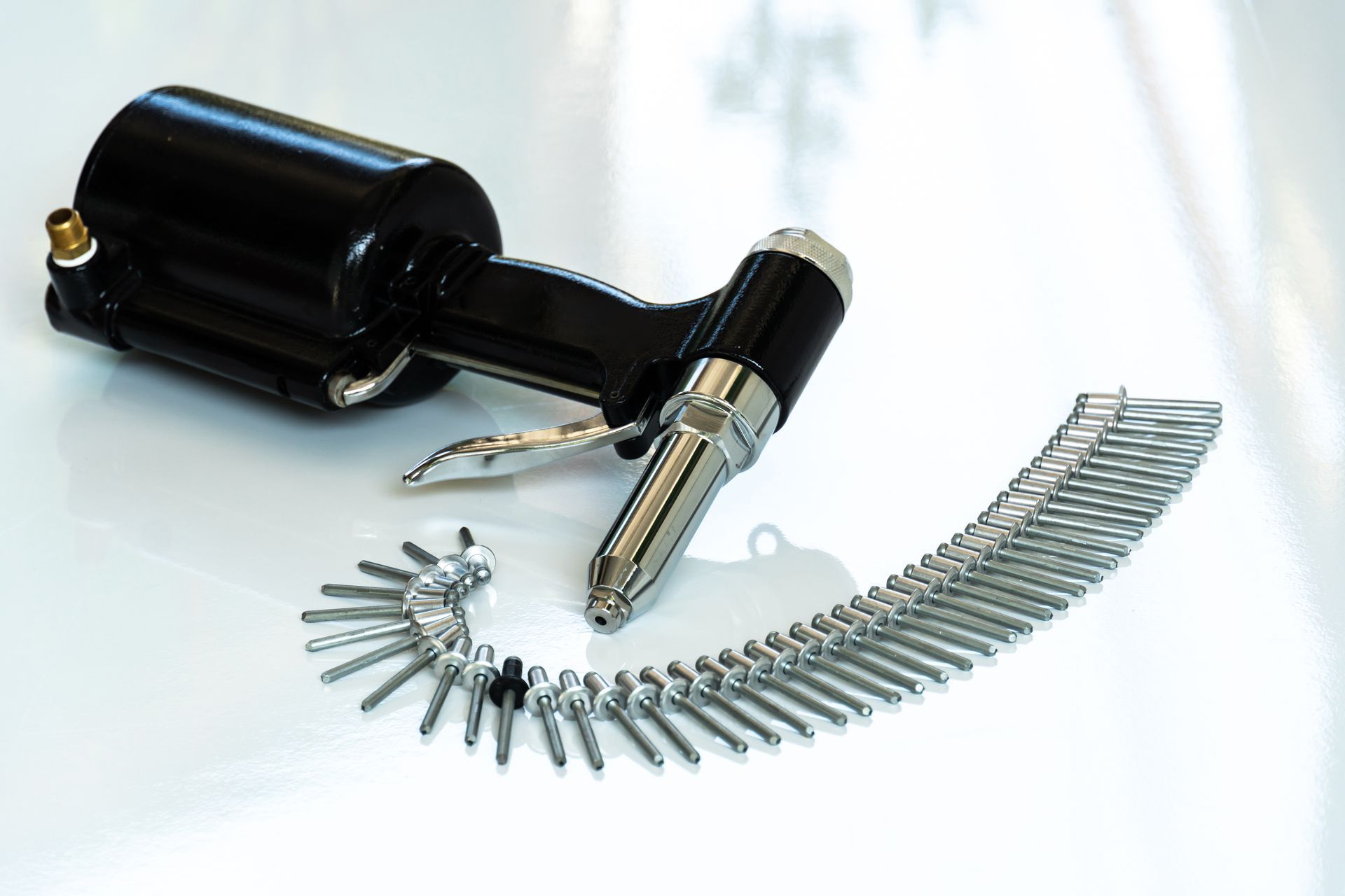 Black pneumatic nail gun with a curved strip of silver nails on a white surface