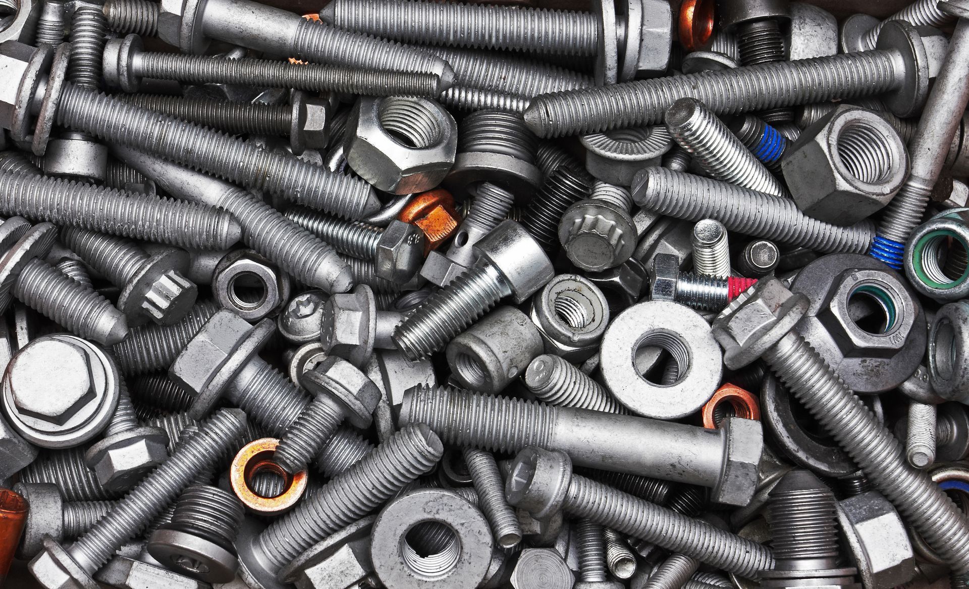 Pile of metal bolts, nuts, and washers scattered in a heap, with a few colored pieces visible.