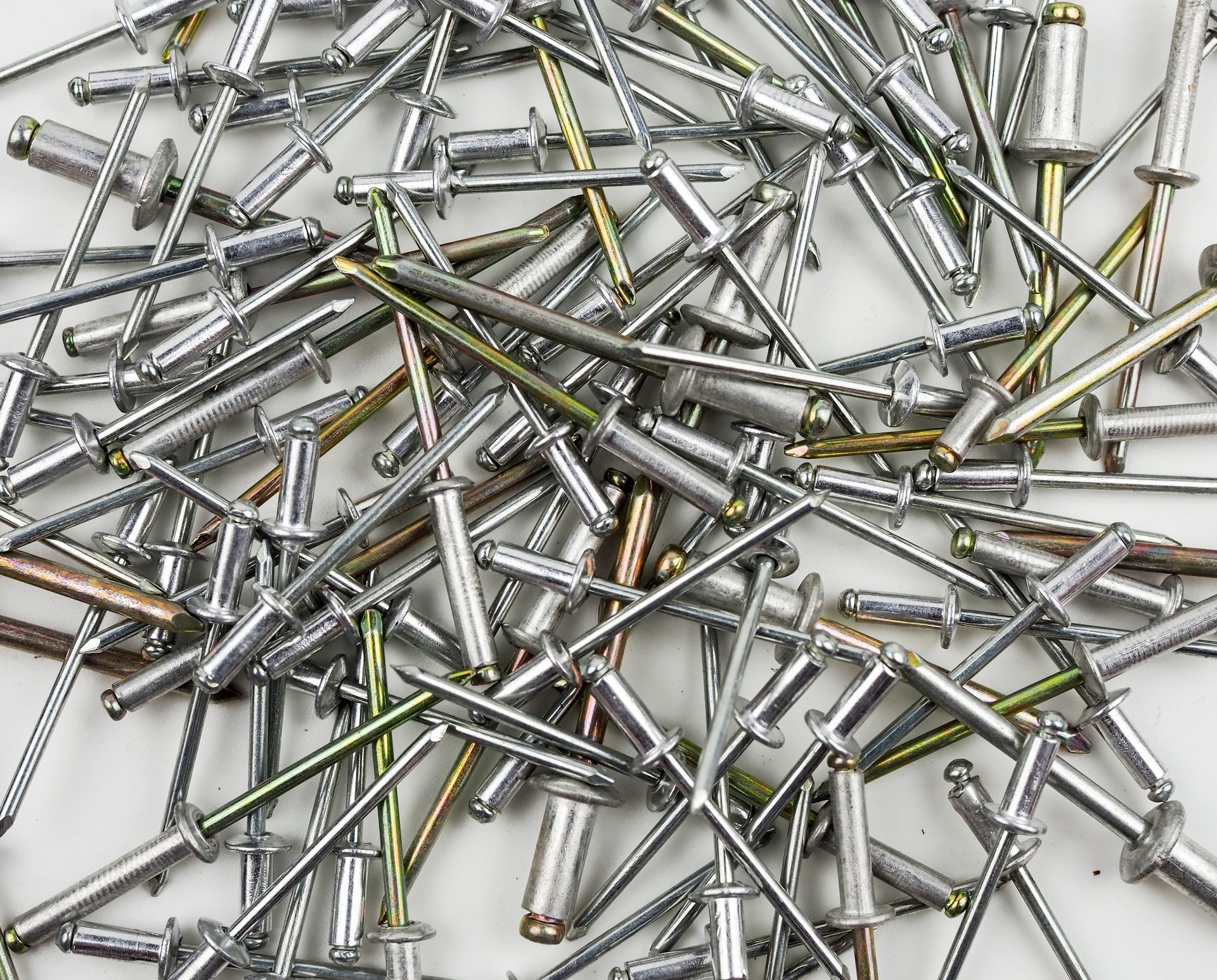 Pile of silver metal screws scattered on a white surface.