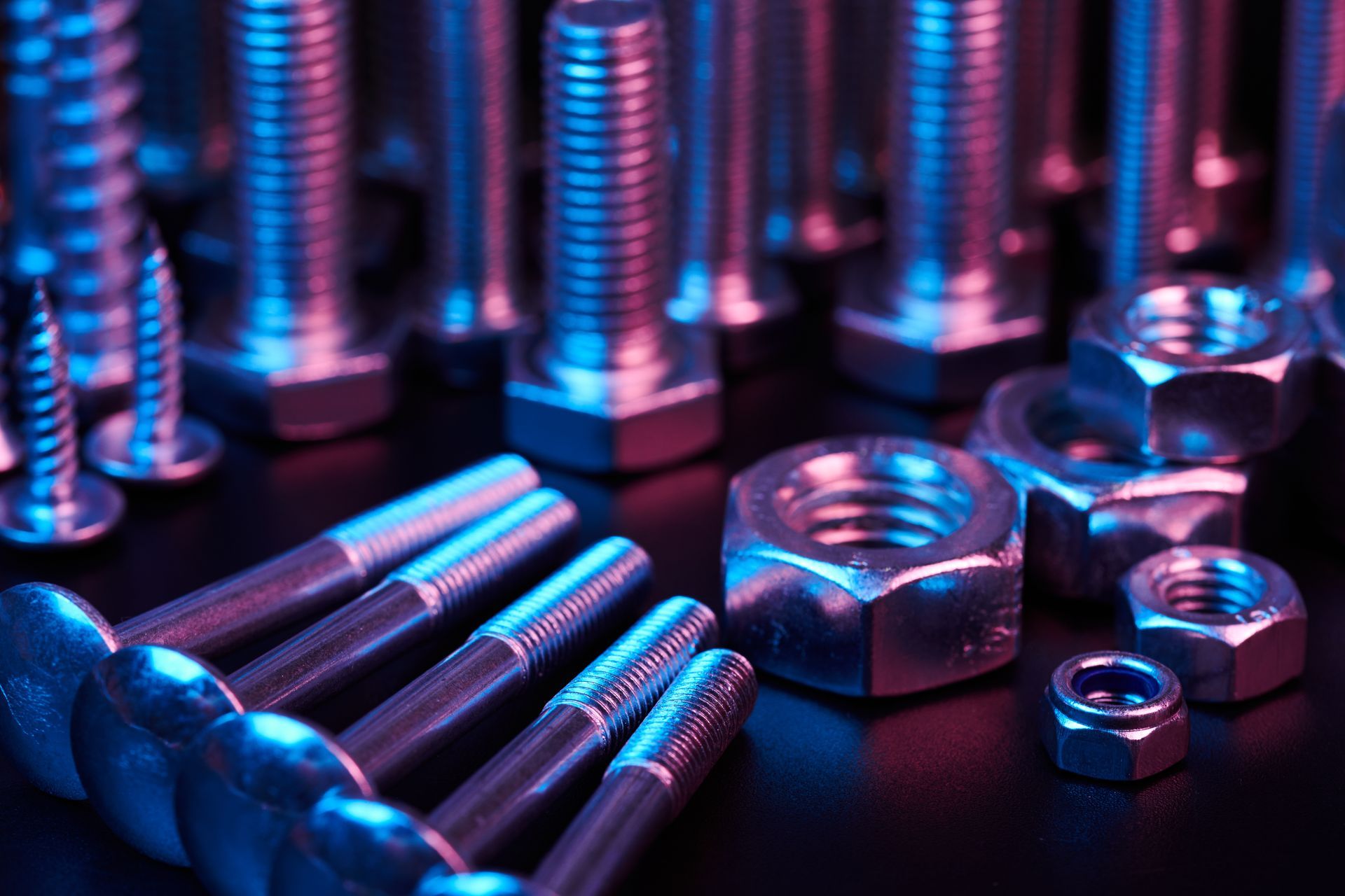 Assorted metal bolts, nuts, and screws on a reflective surface with blue and pink lighting