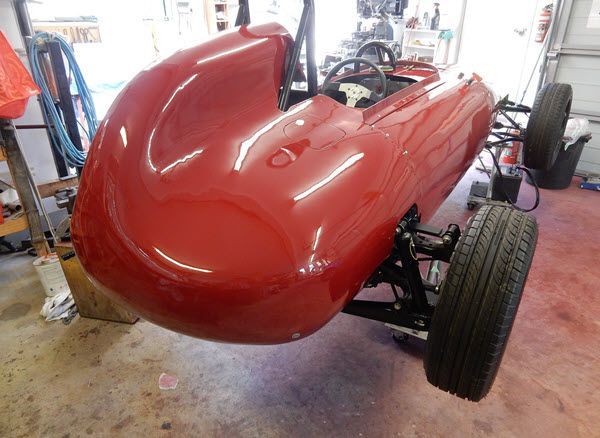 Red vintage race car body in a workshop, front view, glossy red with exposed wheels.