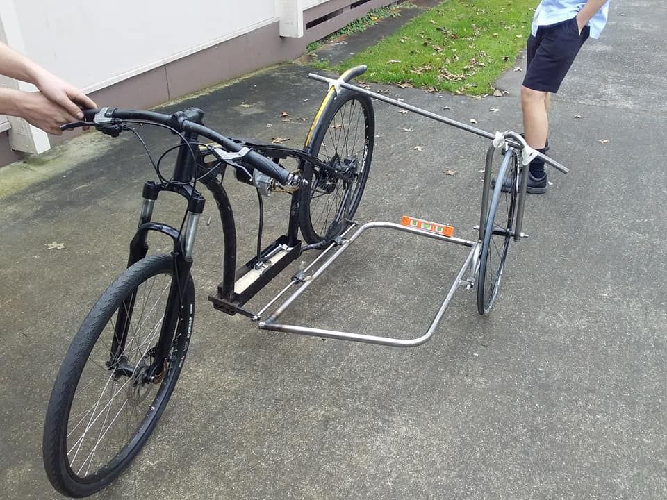 Bicycle towing a child trailer on a wet driveway, with people nearby.