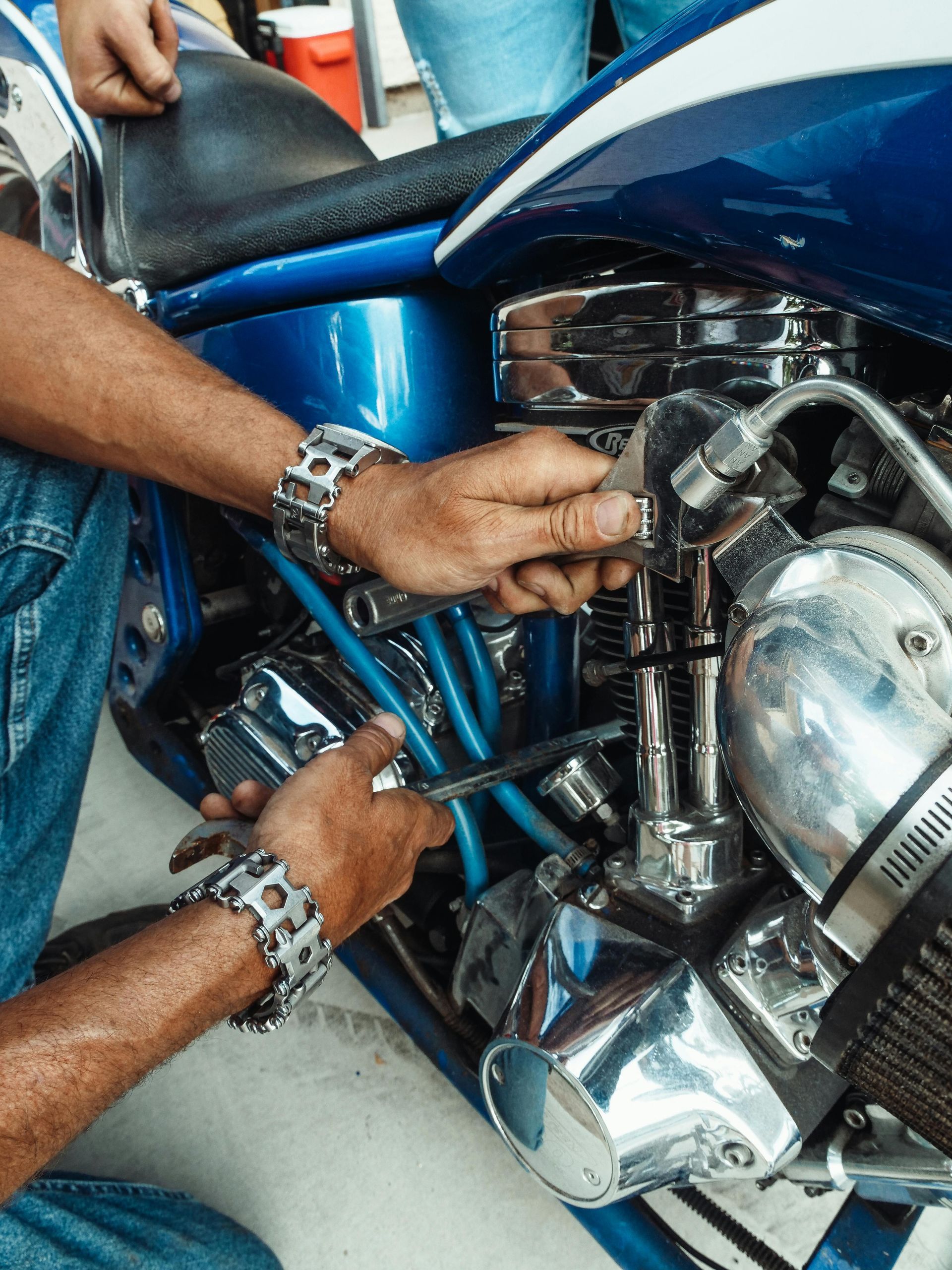Person working on a shiny blue motorcycle engine, wearing a multi-tool bracelet.
