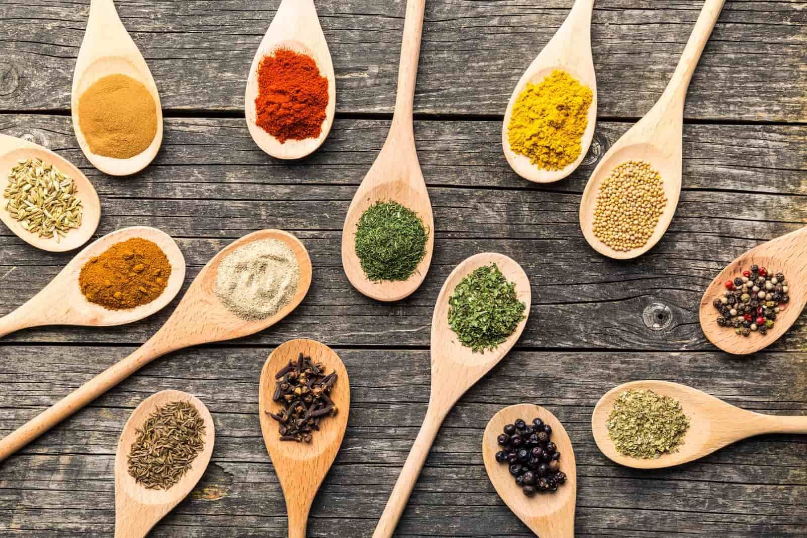 Various spices in wooden spoons on old wooden table. Top view.