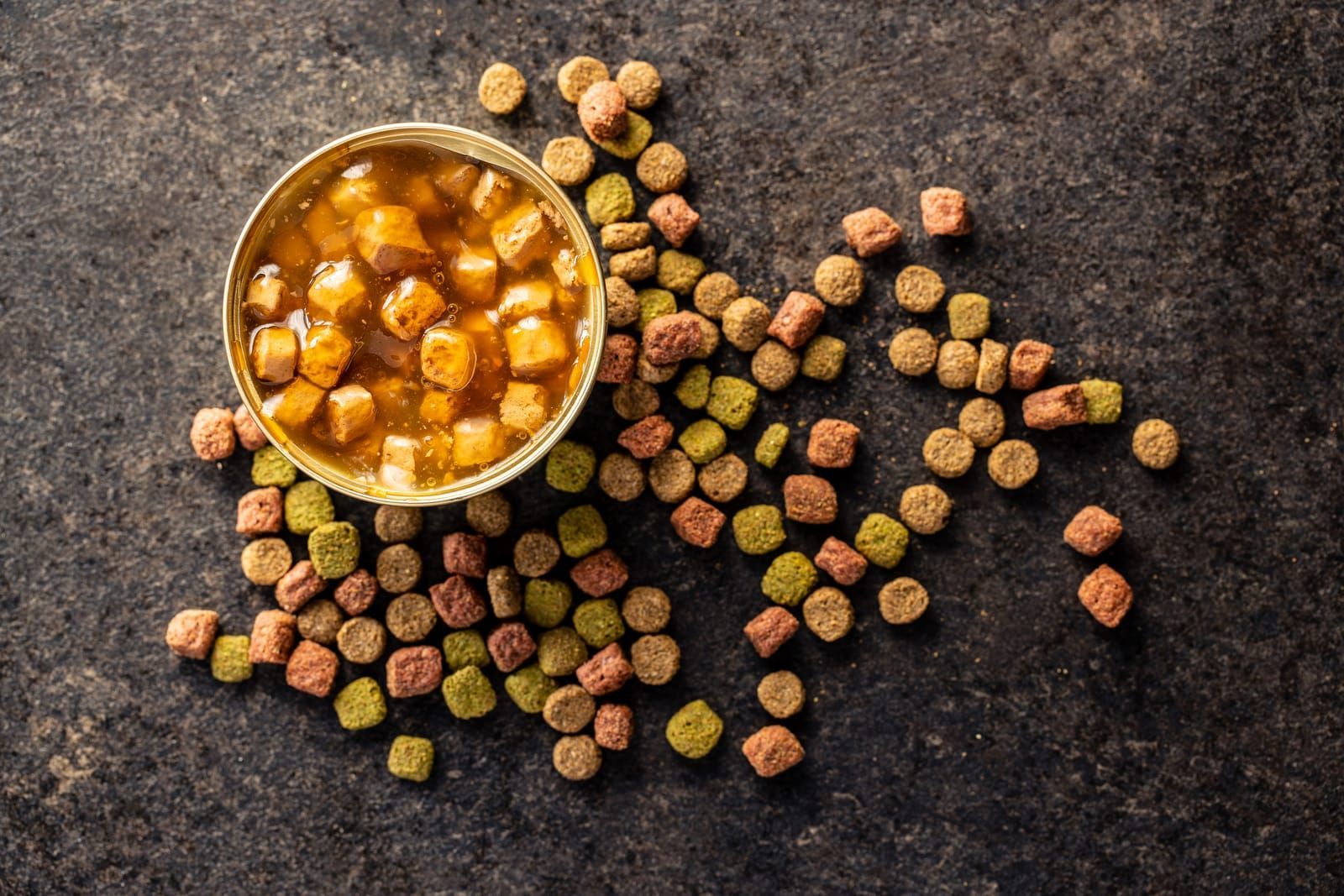 Canned pet food and dried kibble. Tasty food for dog or cat on black table. Top view.