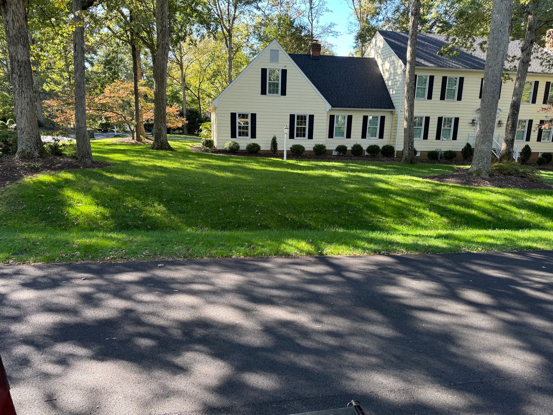 A large white house with a black roof is surrounded by trees and grass.