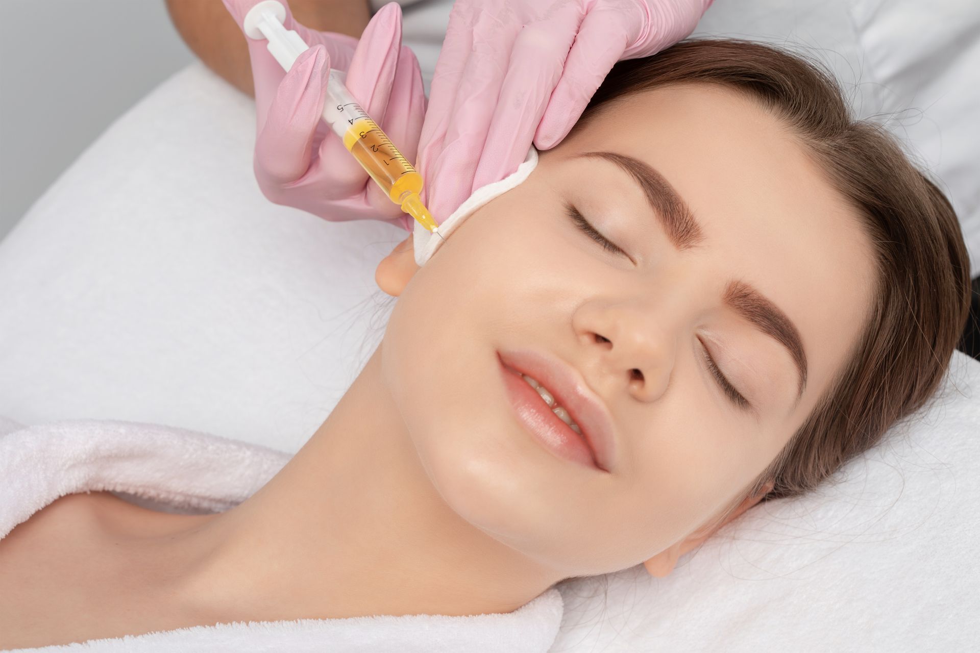Gloved hand injecting serum into a woman’s cheek during a facial treatment