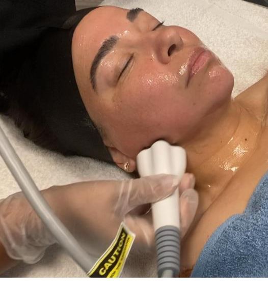 Woman undergoing facial and neck skin treatment with a handheld device in a spa setting.