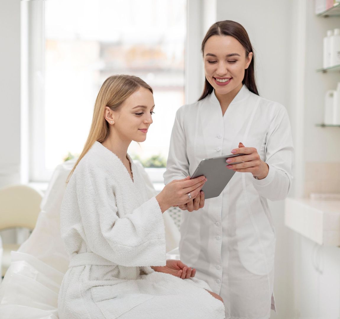 A woman in a robe consults with a medical professional about a tablet in a bright room.