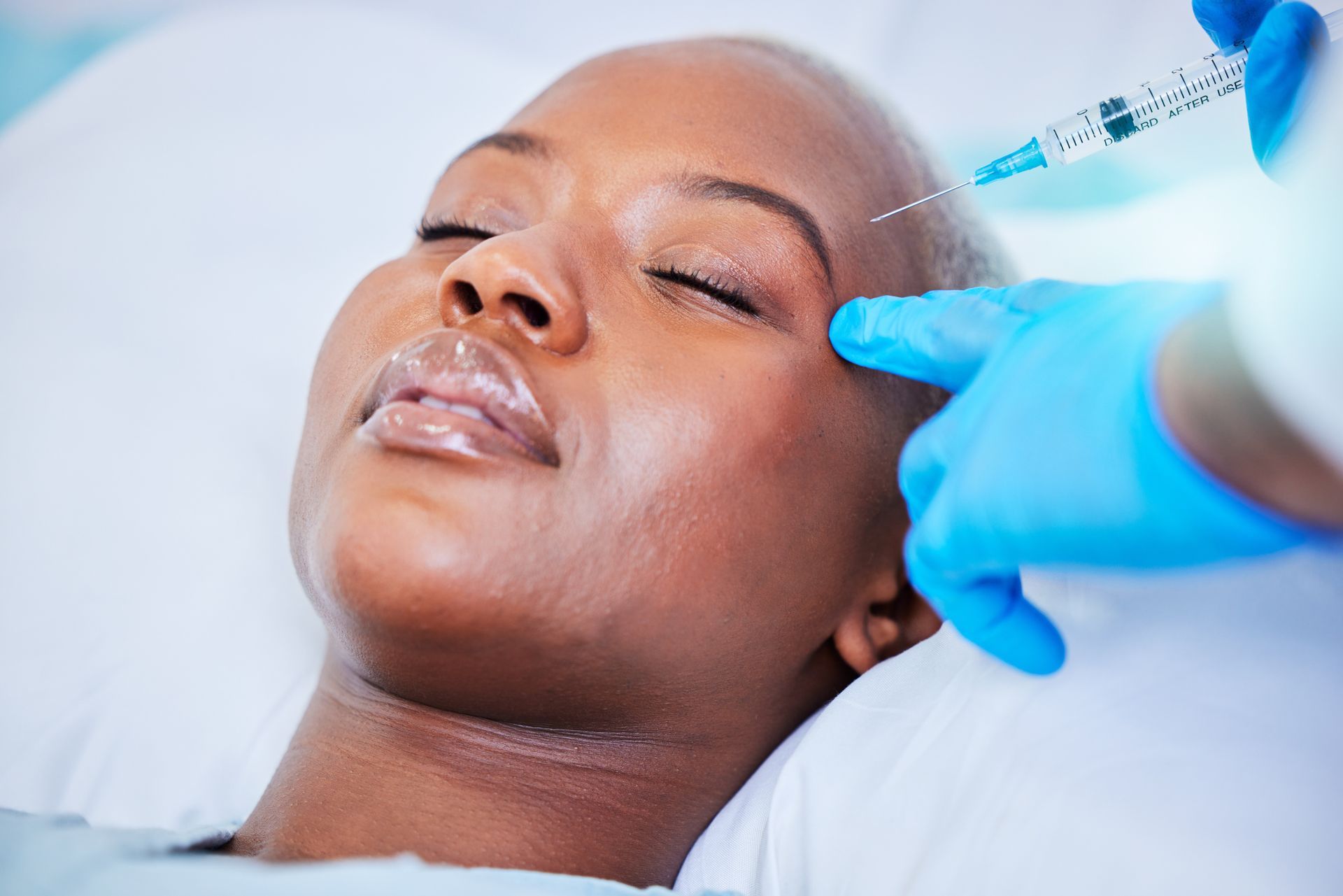 A person receiving a facial injection from a gloved practitioner in a clinical setting