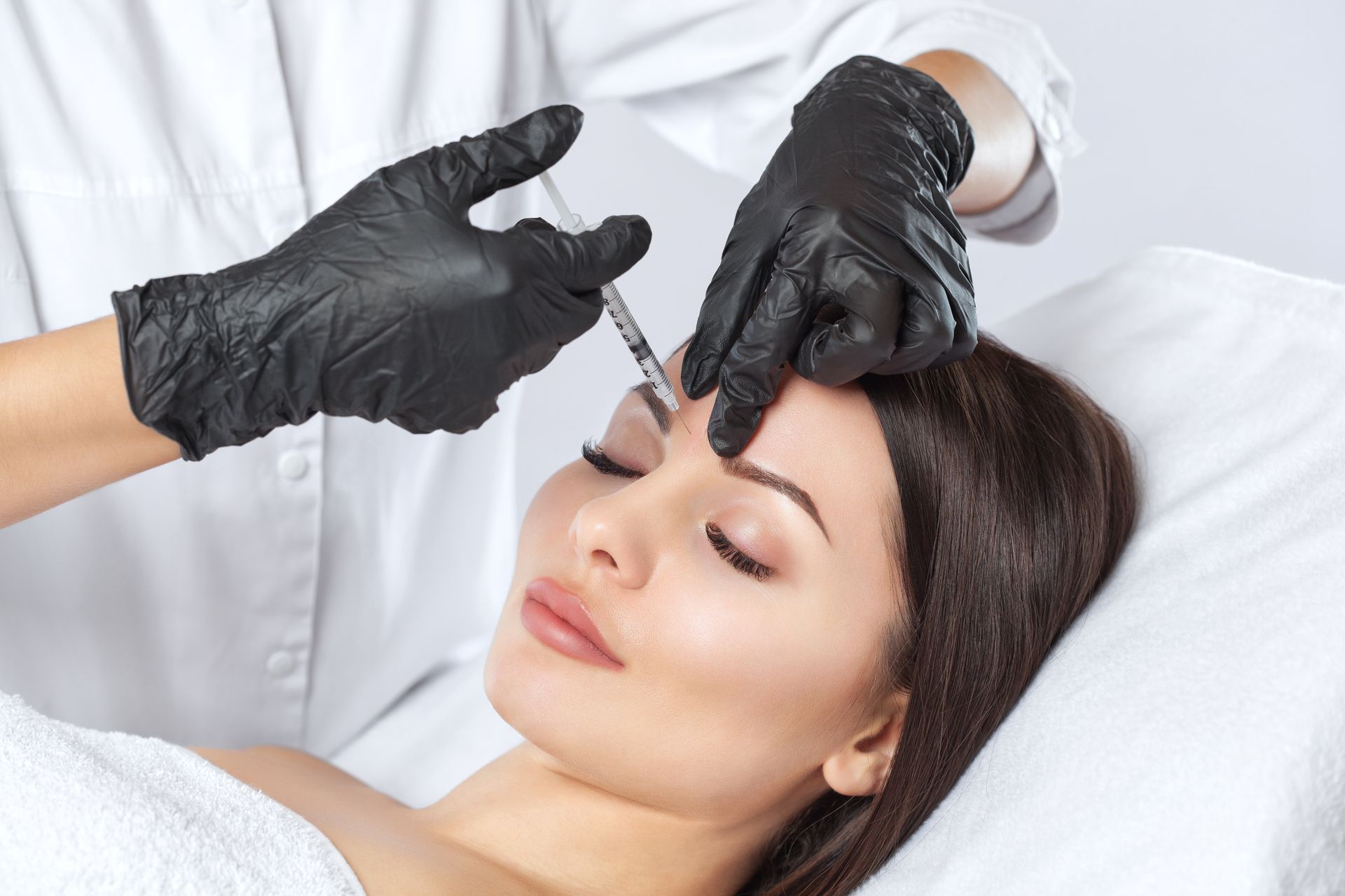 Man receiving cosmetic injections in the face; blue-gloved hands hold a syringe near his eye.