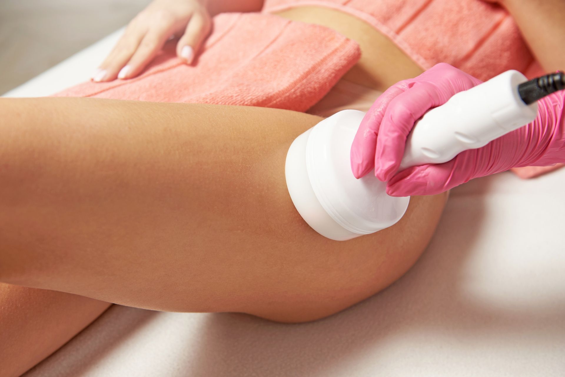 Gloved hand using a white handheld device on a person’s bare thigh during a spa treatment