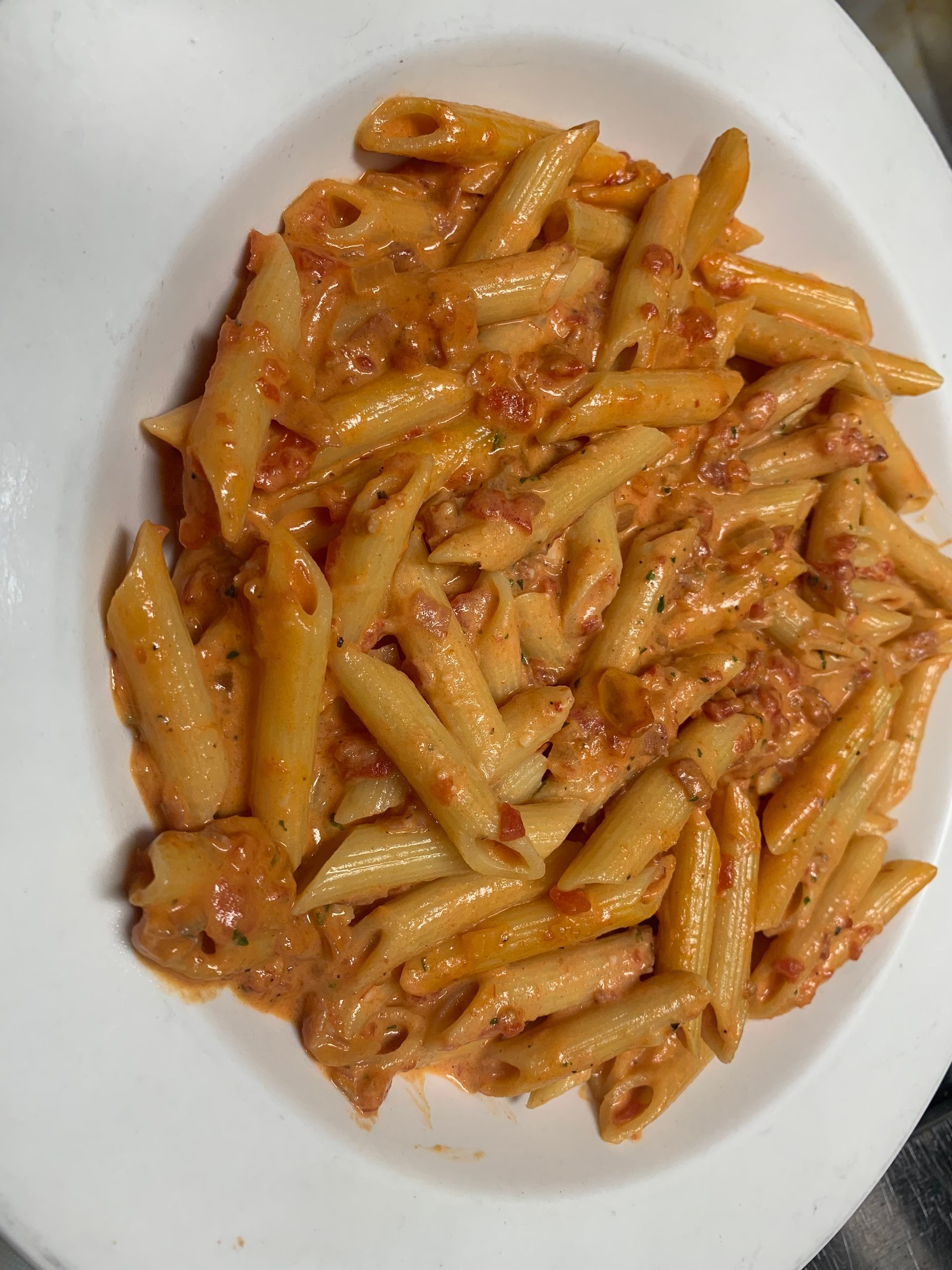 Plate of penne pasta with creamy tomato sauce and bits of meat on a white dish