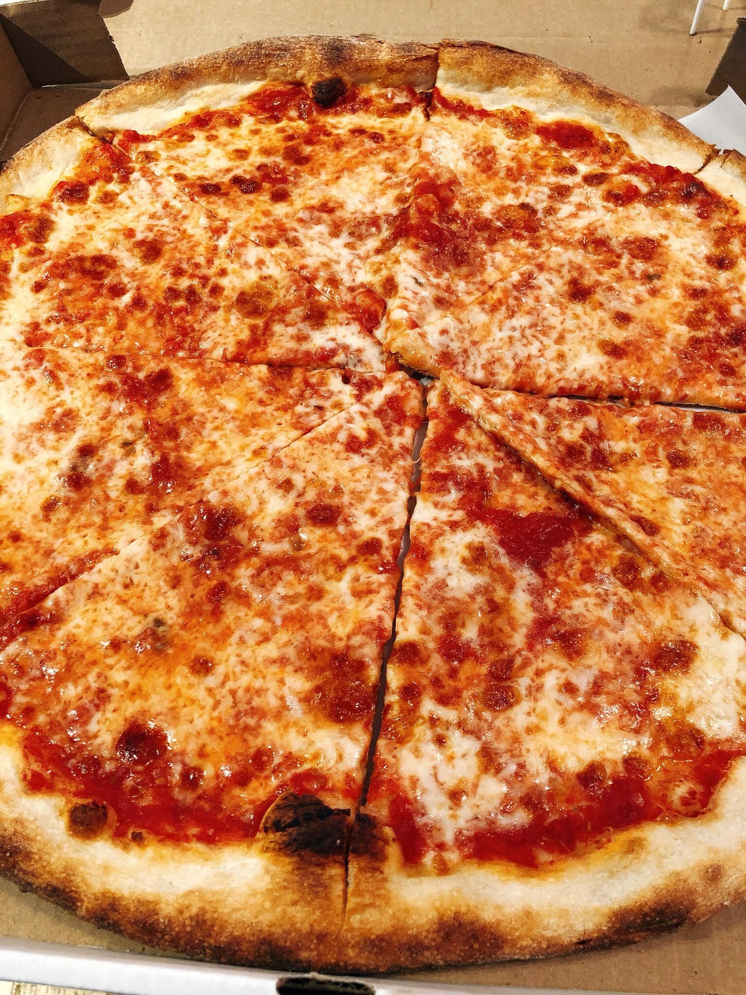 Cheese pizza on cardboard box, cut into slices, with browned crust and tomato sauce showing through