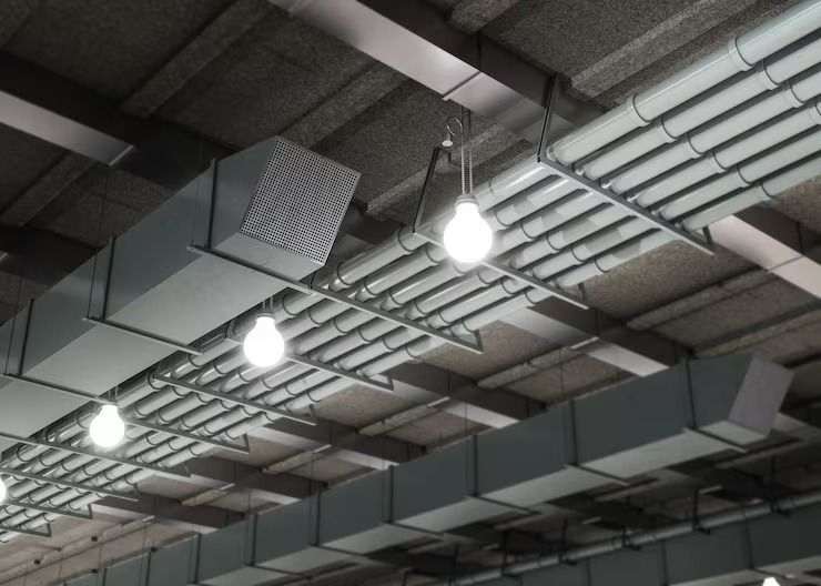 Overhead view of a ceiling with rectangular HVAC ducts, pipes, and hanging light bulbs.