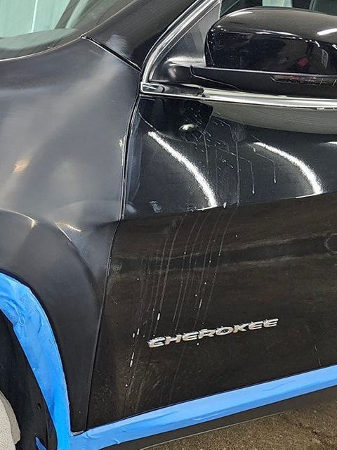 A black jeep cherokee is taped to the ground with blue tape.