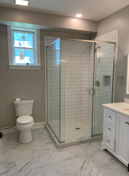 Modern bathroom with glass shower, white toilet, vanity, and marble tile floor
