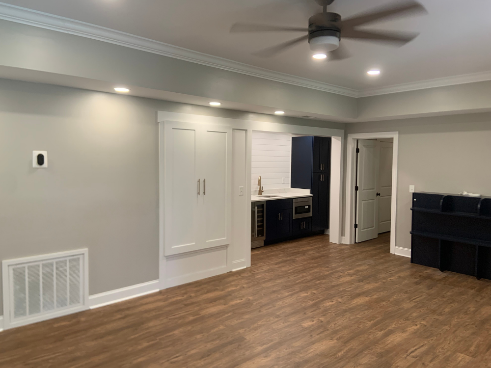 Empty living room with gray walls, wood flooring, ceiling fan, and built-in white cabinets.