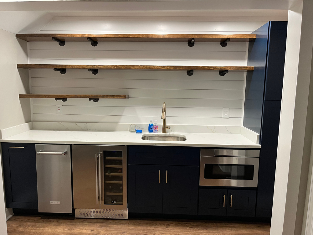 Modern kitchenette with black cabinets, wood shelves, sink, mini fridge, wine cooler, and microwave.