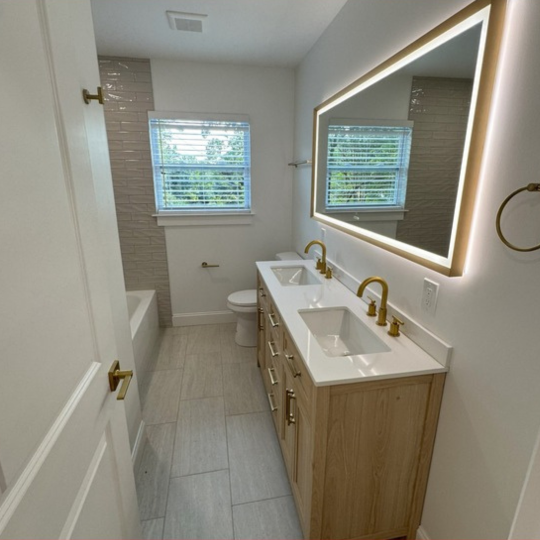 Bathroom with double vanity, gold fixtures, large mirror, and wood cabinet.