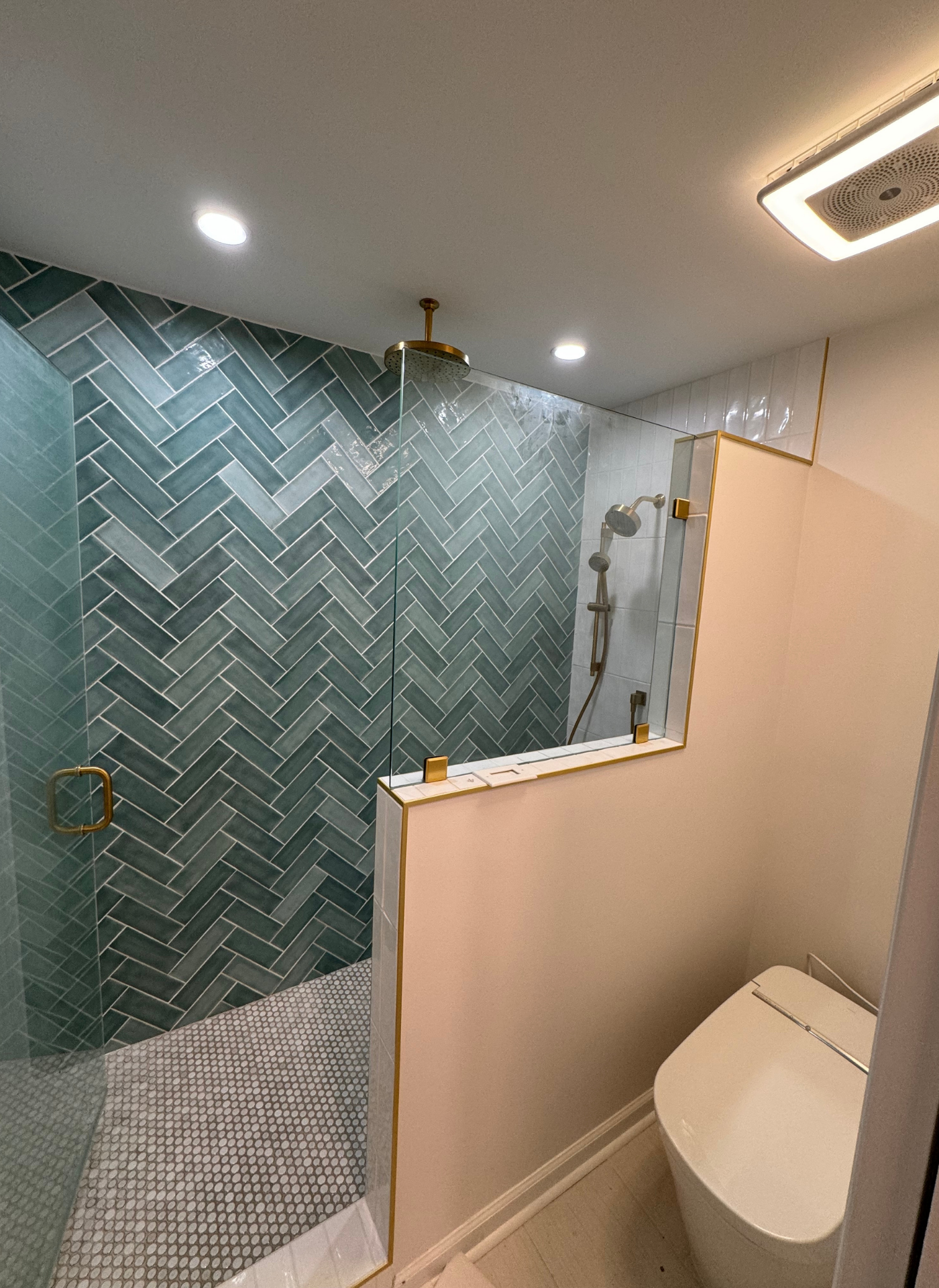 Modern bathroom with green tile shower, beige half wall, and toilet in the foreground