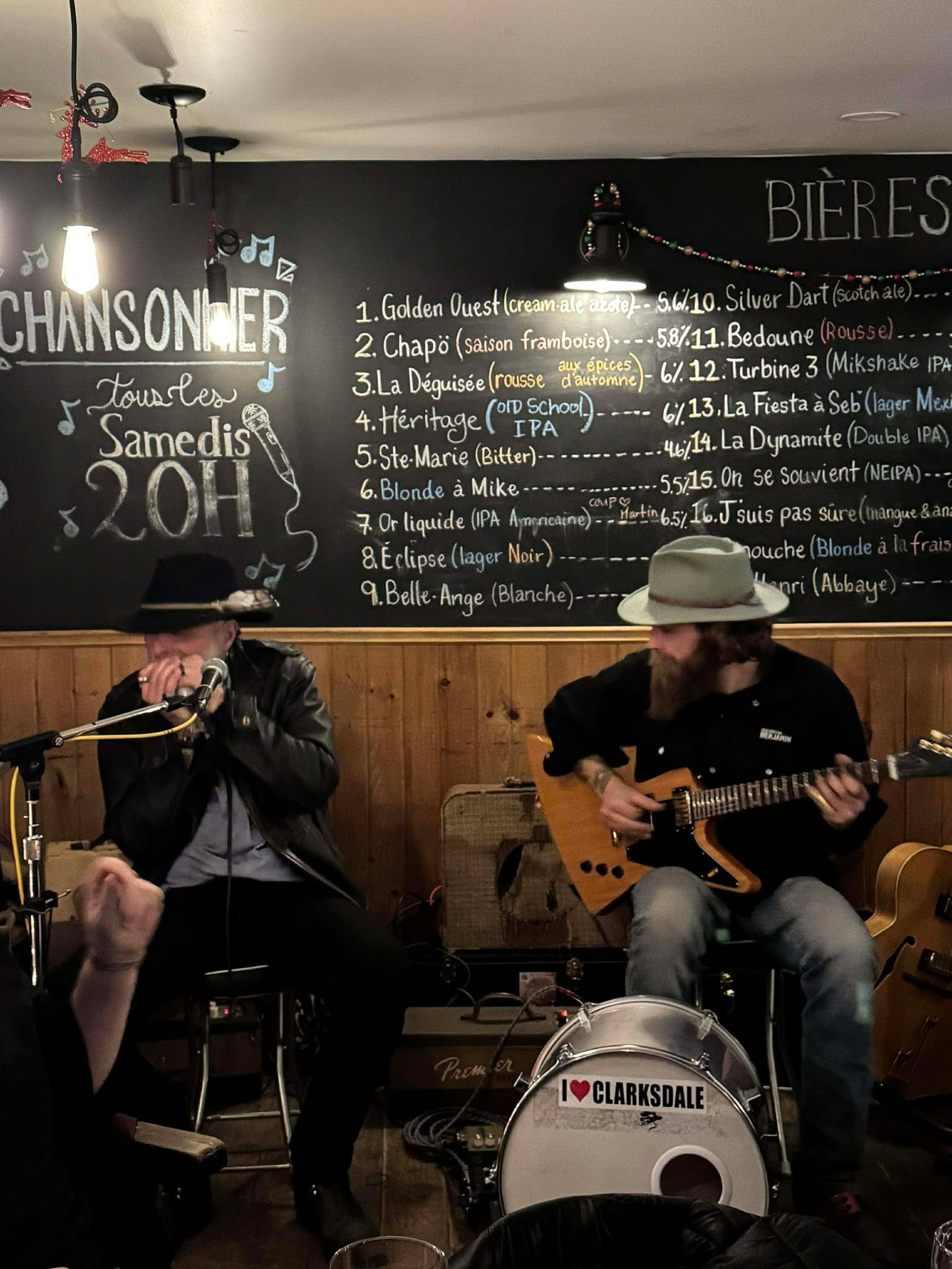 Two musicians sitting , one playing a guitar and another playing the harmonica