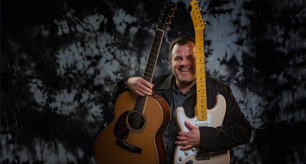 Adam Karch holding an electric and acoustic guitar