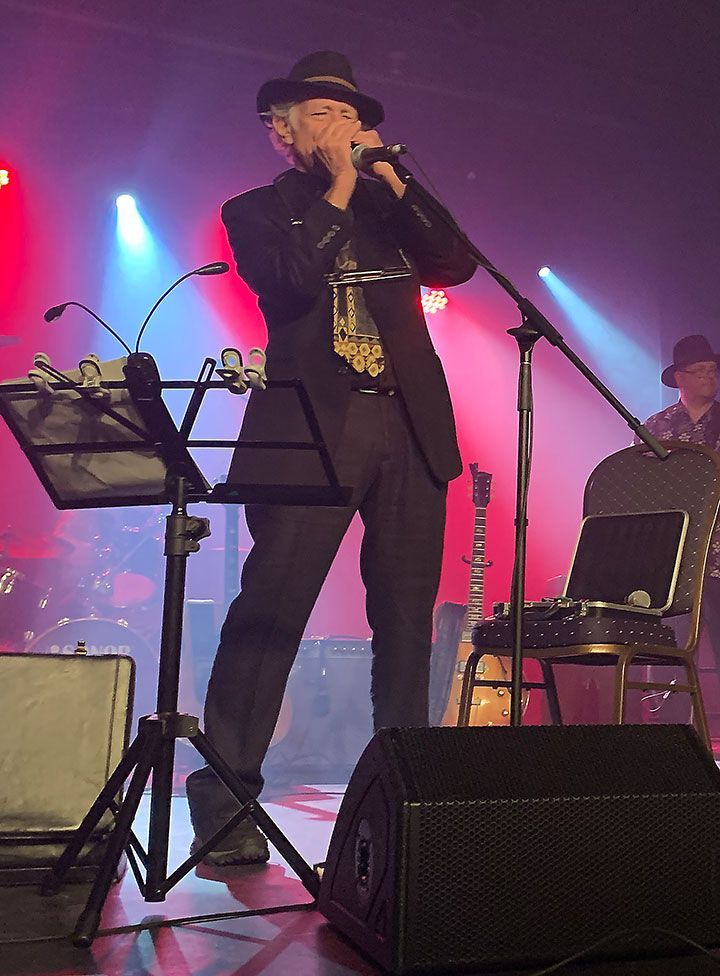 Jay Sewall playing harmonica on stage with microphones and musical instruments all around him