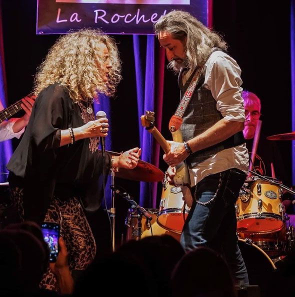 Femme sur scène tenant un micro, face à face avec un guitariste