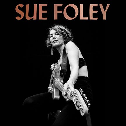 An image of Sue Foley holding a guitar with a pitch black background.
