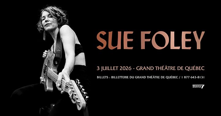 Sue Foley holding an electric guitar against a black background.