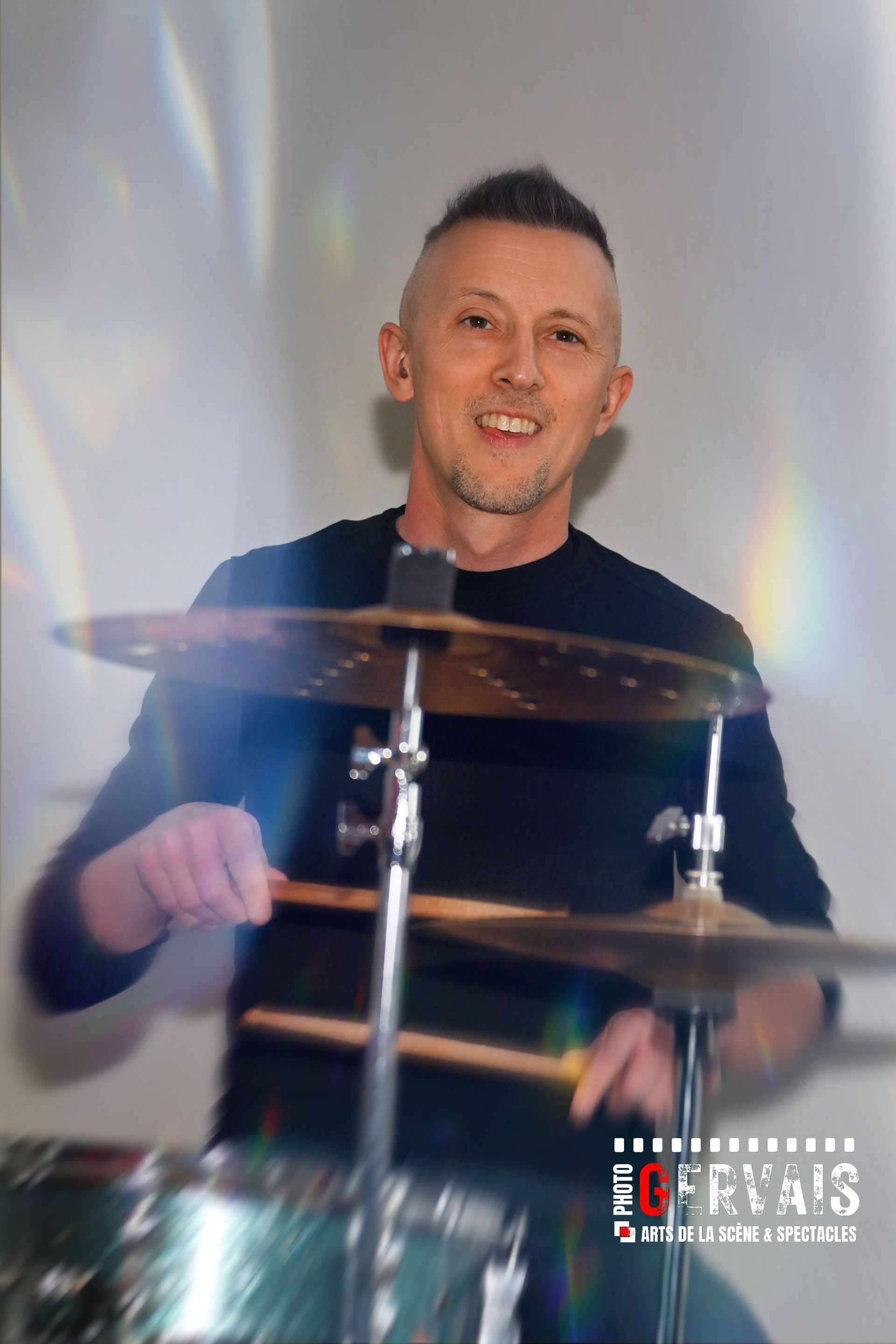 A man smiling playing a set of drums