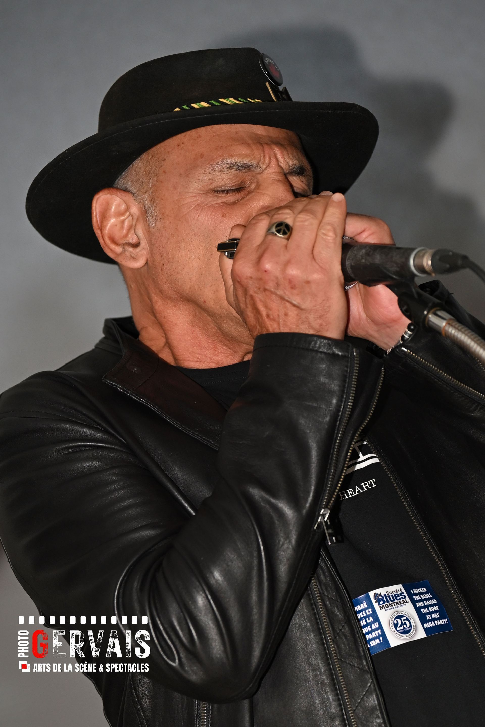 A man in a black hat and leather jacket playing harmonica