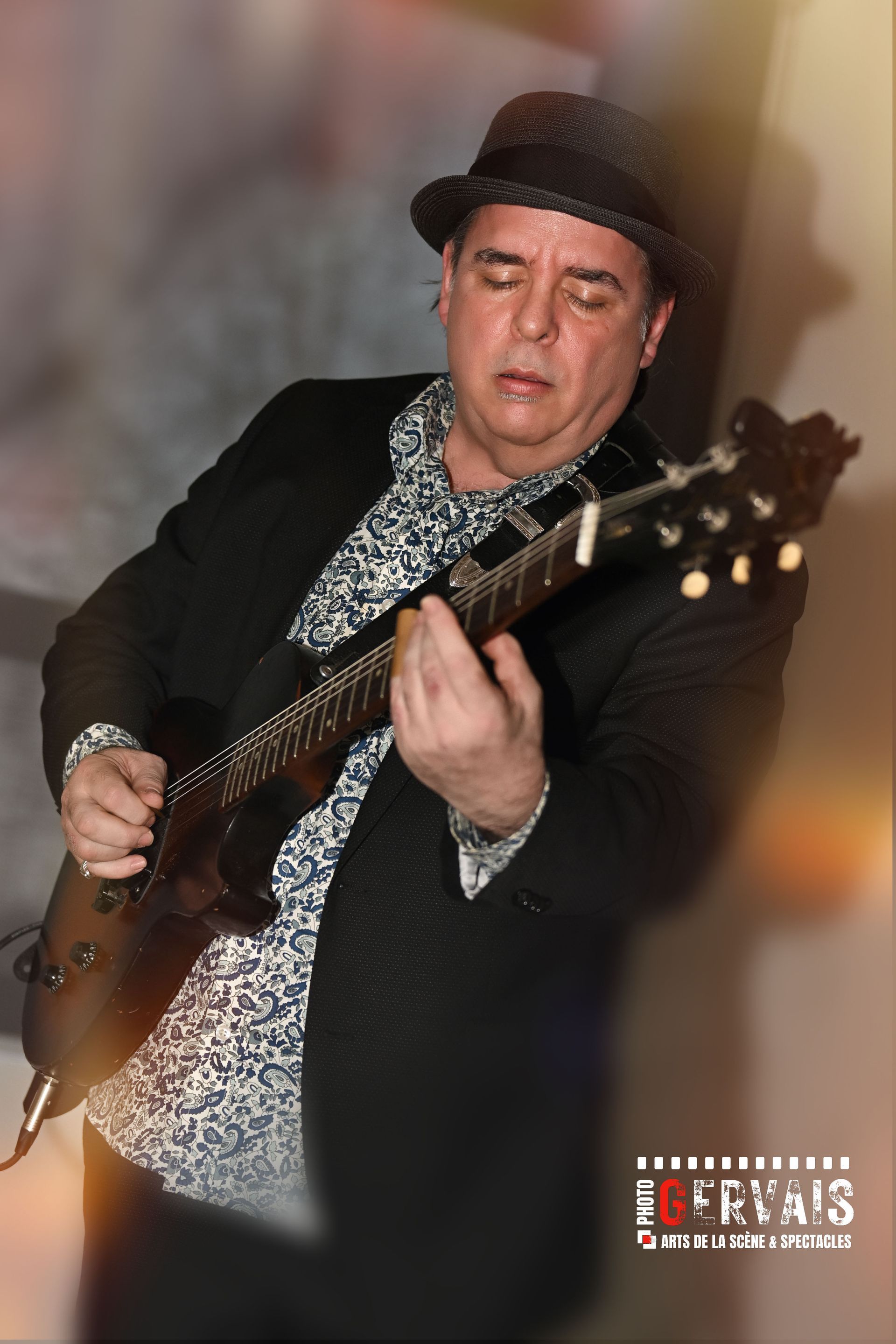 A different man wearing a black hat and a white and black shirt playing guitar