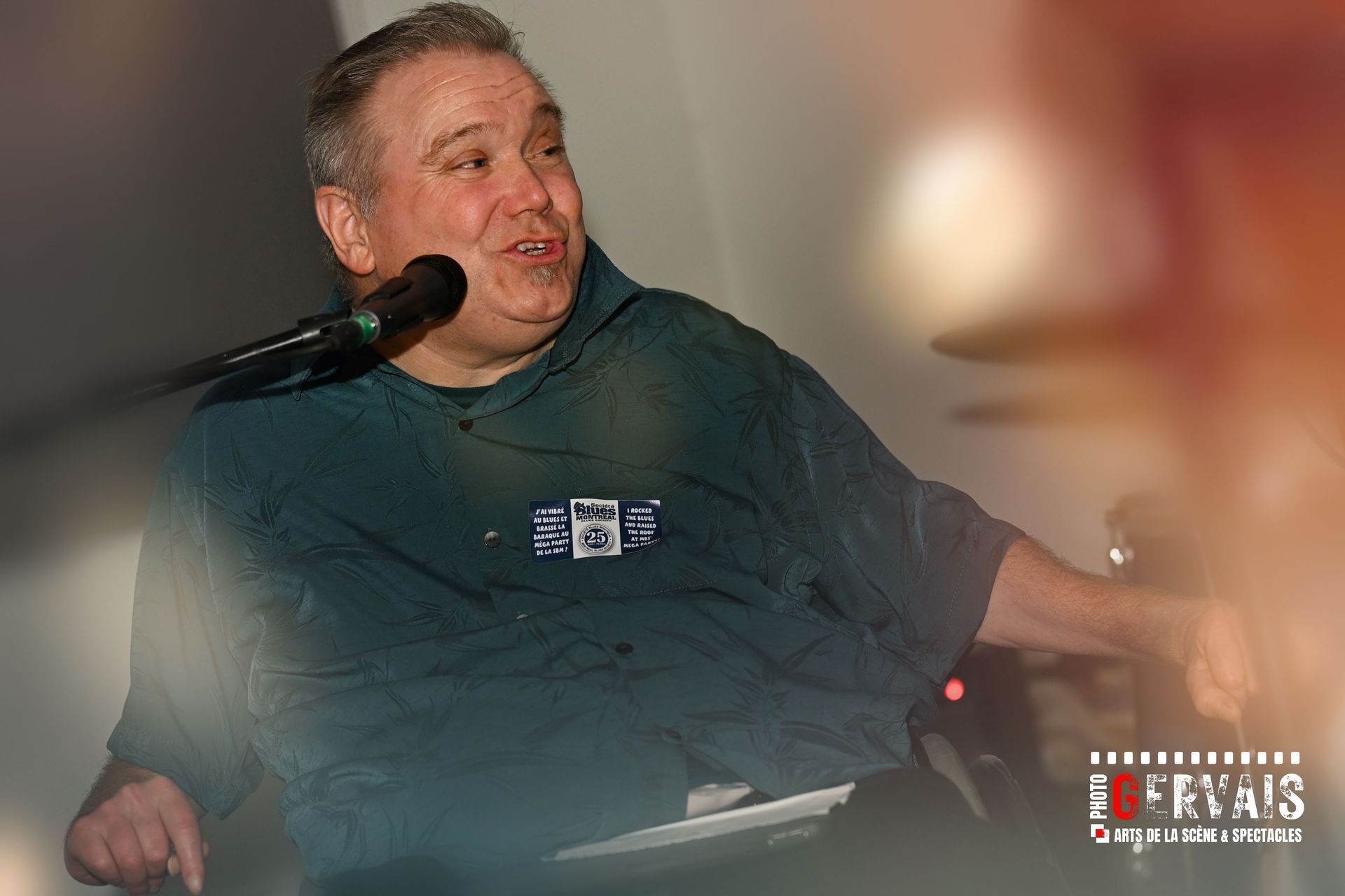 A man in a wheelchair wearing a green t-shirt smiling and singing