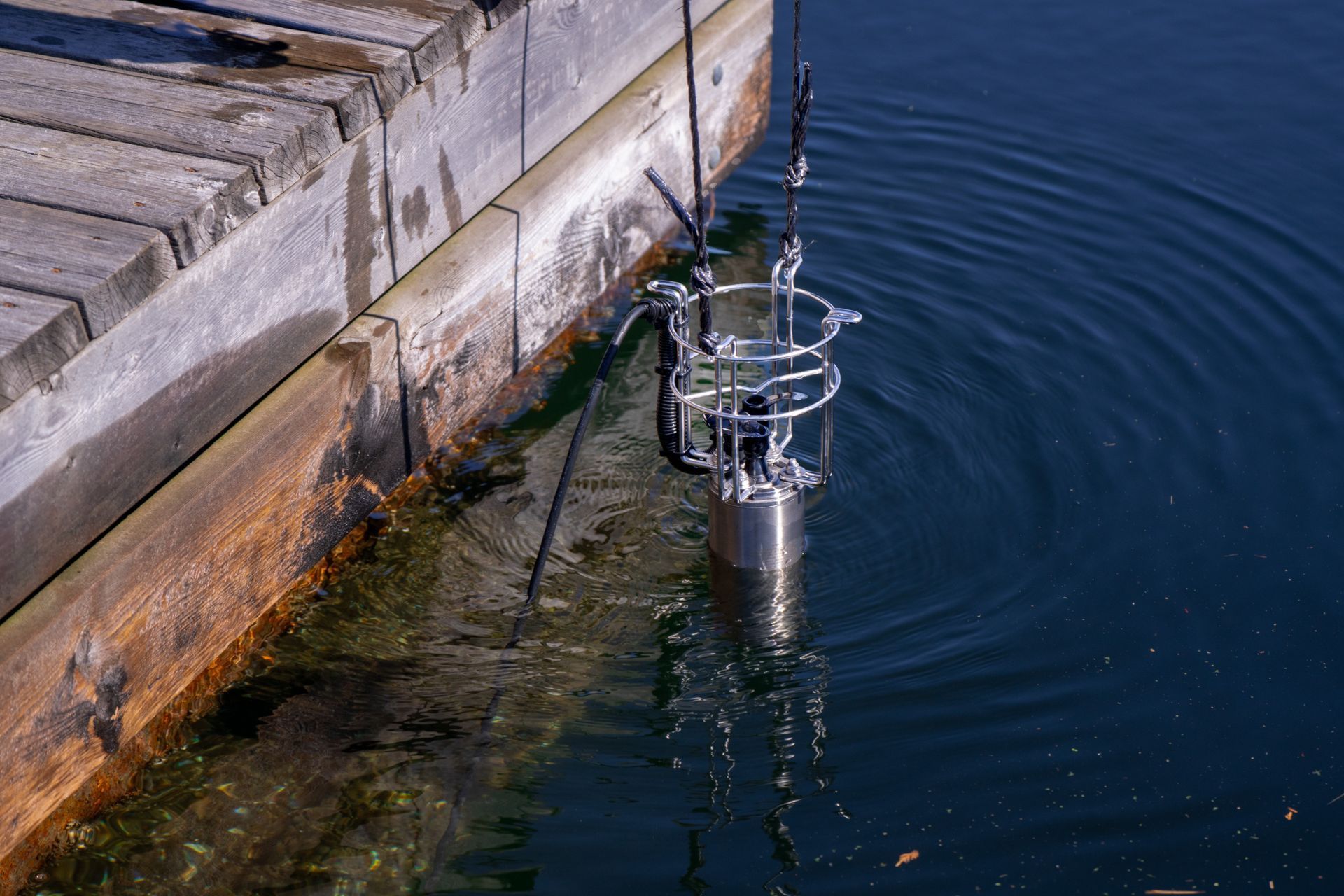 Metal instrument lowered into water from a wooden dock, used for de-icing and cleaning waterfronts
