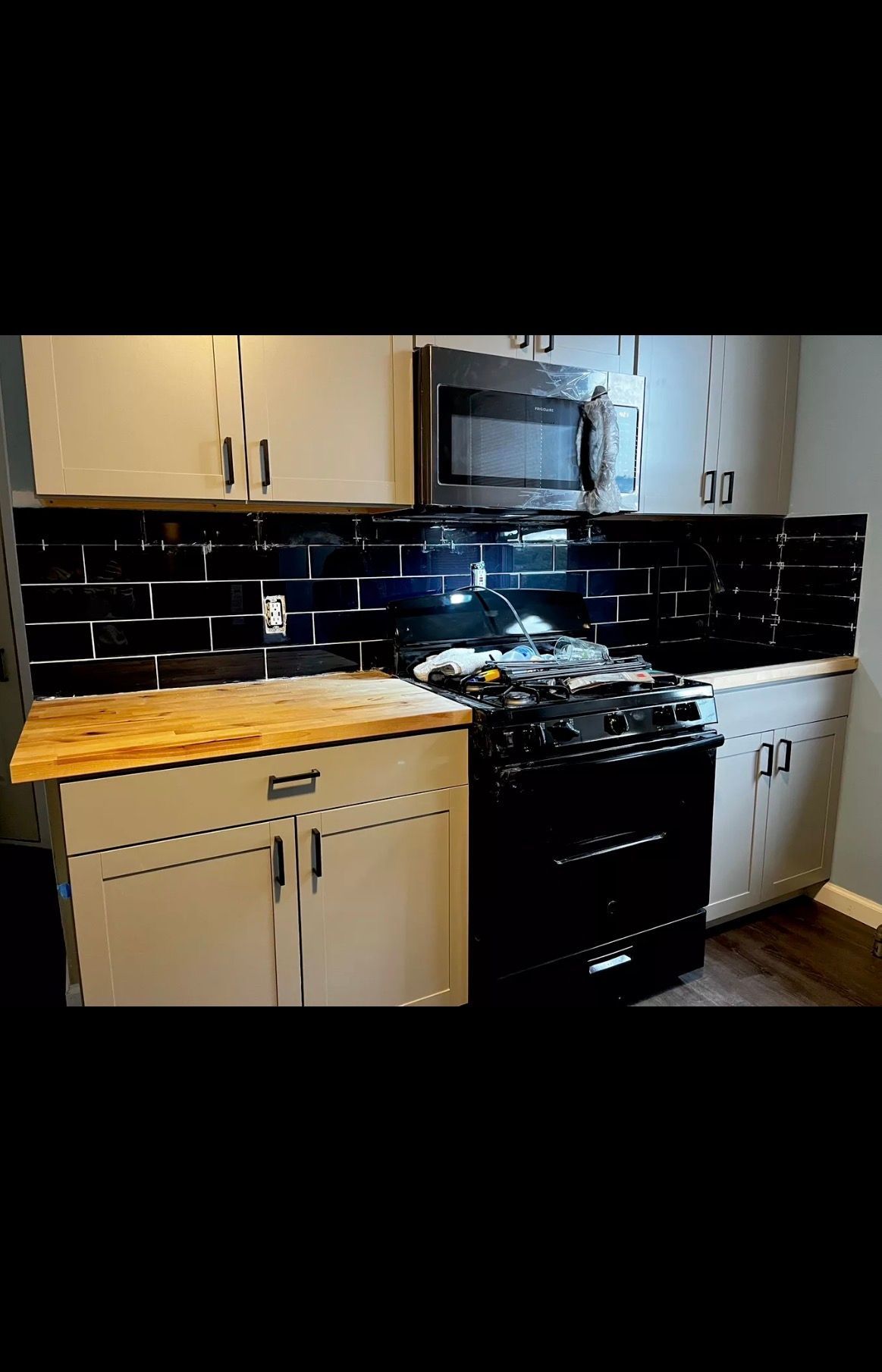 A kitchen featuring white cabinets, a light wood countertop, a black gas stove with a matching microwave, and black tiles.