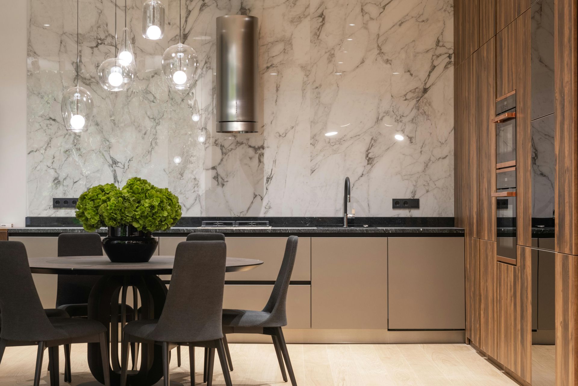 A modern kitchen with marble backsplash, wooden cabinets, and a dining table with a green floral centerpiece.